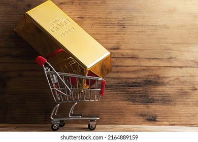 Closeup Shot Of A Large Shiny Gold Bar Put In A Tiny Shopping Cart With Wooden Wall Background.