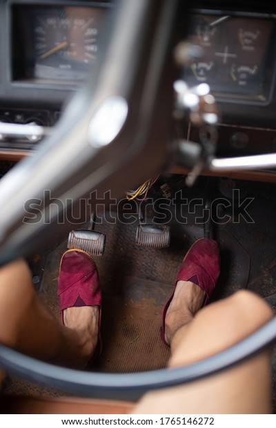 A closeup shot of male feet in\
purple cloth shoes pushing on gas and break pedals in an old\
car