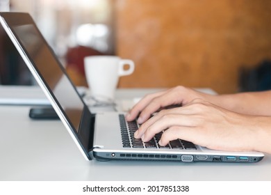 Close-up Shot Of Male Hands Typing On A Laptop While Sitting At Office Desk Indoors, Man Fingers Tapping And Texting On Computer Keyboard While Working In The Cabinet, Work Concept.