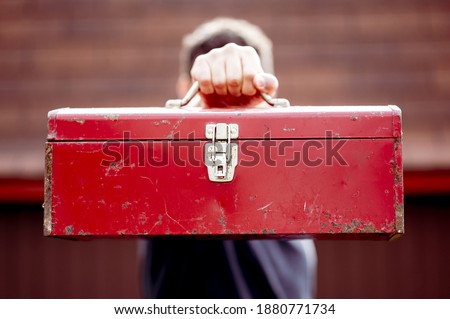 A closeup shot of a male holding a toolbox in front of his fa