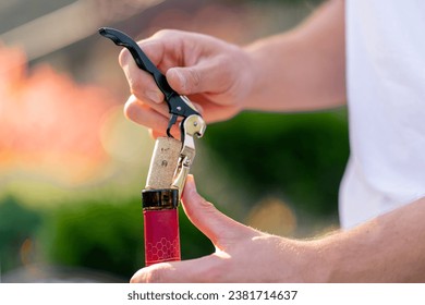 Close-up shot of a male sommelier's hand using a corkscrew to unscrew the wooden cork of a wine bottle