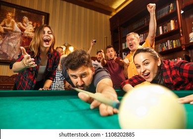 Close-up shot of a man playing billiard. The caucasian model carefully and strenuously aiming by cue in the ball. Game concept. Human emotions and facial expression concepts. Friends as background - Shutterstock ID 1108202885