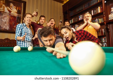 Close-up shot of a man playing billiard. The caucasian model carefully and strenuously aiming by cue in the ball. Game concept. Human emotions and facial expression concepts. Friends as background - Shutterstock ID 1108202891