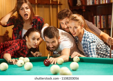 Close-up shot of a man playing billiard. The caucasian model carefully and strenuously aiming by cue in the ball. Game concept. Human emotions and facial expression concepts. Friends as background - Shutterstock ID 1108203056