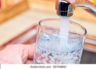 Closeup shot of a man pouring a glass of fresh water from a kitchen faucet - Shutterstock ID 587948843