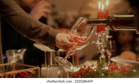 Close-up shot of man pours wine into wine glass. Family celebrating Christmas, New Year or Thanksgiving Day. Served table with dishes and candles. Warm atmosphere of family Christmas dinner at home. - Powered by Shutterstock