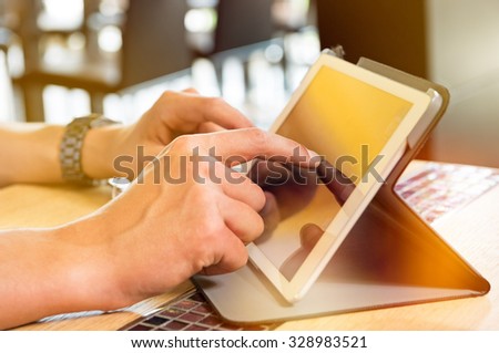 Closeup shot of man using digitaltablet. Guy is touching screen of tablet at cafe. Detail of a young man's hand typing on digital tablet at restaurant.
