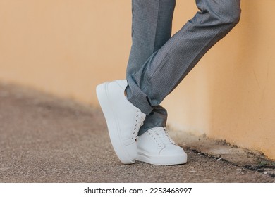 A close-up shot of a man wearing white sneakers with gray classic pants