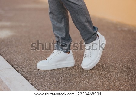 A close-up shot of a man wearing white sneakers with gray classic pants