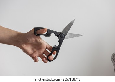 A Closeup Shot Of A Man's Arm Holding Black Scissors Against White Wall