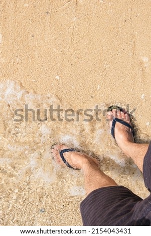 Close-up shot of man's legs in flip-flops while standing by the sea