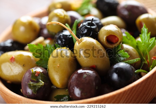 Close-up shot of marinated olives with herbs and\
spices in wooden\
plate.