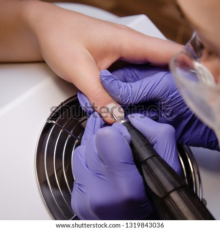 Closeup shot of master in rubber gloves applying an electric nail file drill to trim and remove cuticles in the beauty salon. Perfect nails manicure process. Hardware manicure