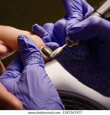 Closeup shot of master in rubber gloves applying an electric nail file drill to remove the nail polish in the beauty salon. Perfect nails manicure process with flying dust or debris