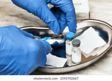 Close-up shot of medical assistant wearing protective gloves holding syringe preparing for vaccination with vaccine vials and supplies in a medical tray - Powered by Shutterstock