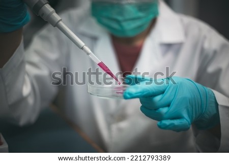 Closeup shot of a medical researcher using a micropipette to add drops of developed red drug liquid in testing the biological activity with culture cells in a laboratory.