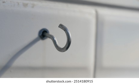 A close-up shot of a metal hook screwed into a wall. The hook is curved at the end, suggesting it is designed to hold objects. The background appears to be a tiled surface. - Powered by Shutterstock