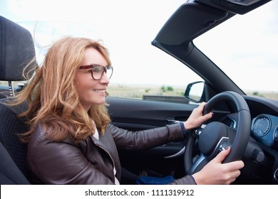 Close-up Shot Of Middle Aged Woman Driving Her Cabriolet Sport Car On The Road. 