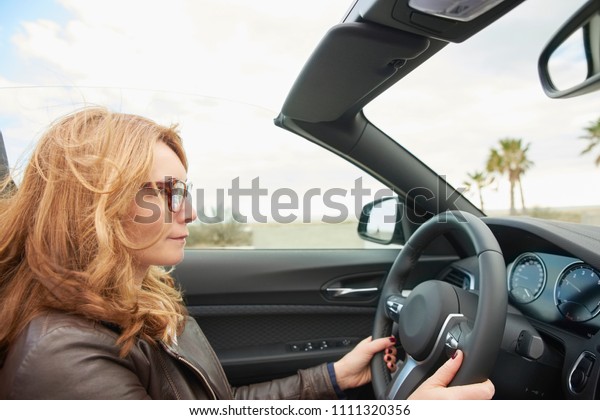 Close-up shot of middle aged woman driving her\
cabriolet sport car on the road.\
