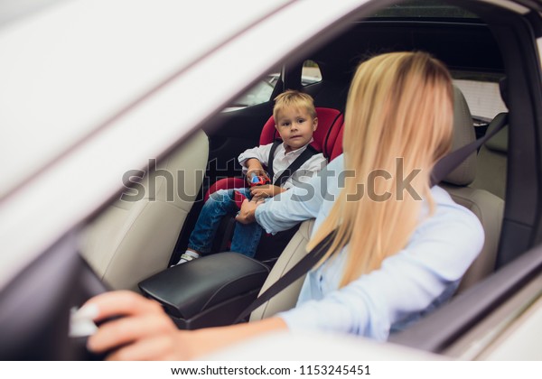 Close-up shot mother\
driving car, buckled seat belt. Son on back seat. Family holding\
their thumbs up