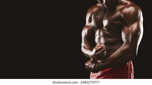 A close-up shot of a muscular man flexing his biceps, showcasing his defined physique. He is wearing red shorts and standing against a black background. - Powered by Shutterstock