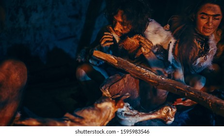 Close-up Shot of Neanderthal or Homo Sapiens Family Cooking Animal Meat over Bonfire and then Eating it. Tribe of Prehistoric Hunter-Gatherers Wearing Animal Skins Eating in a Dark Scary Cave at Night