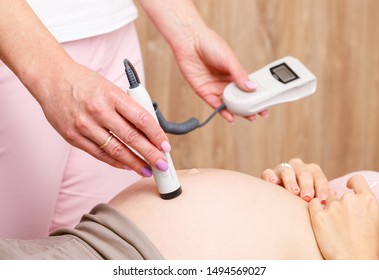 Close-up Shot Of Obstetrician Gynecologist Performing Doppler Auscultation Checking Blood Flow In Placenta And Uterus With Doppler Fetal Monitor During Prenatal Checkup