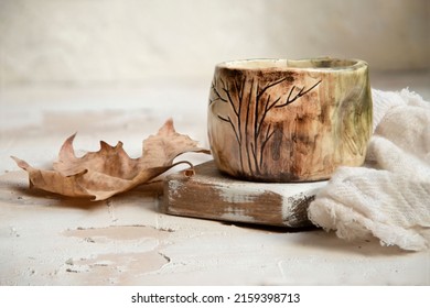 A Closeup Shot Of An Old Ceramic Mug On A Wooden Surface With A Cloth And Dried Leaf On The Side