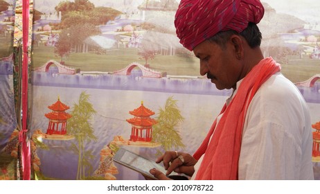 A Closeup Shot Of An Old South Asian Man Wearing A Traditional Costume And Typing On A Tablet