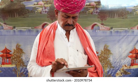 A Closeup Shot Of An Old South Asian Man Wearing A Traditional Costume And Typing On A Tablet