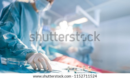 Close-up Shot in Operating Room of Surgical Table with Instruments, Assistant Picks up Instruments for Surgeons During Operation. Surgery in Progress. Professional Medical Doctors Performing Surgery.