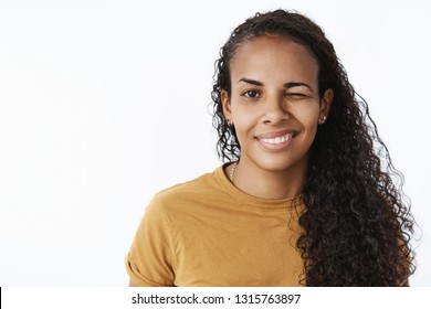 Close-up shot of optimstic and confident good-looking dark-skinned girl with curly hairstyle winking at camera with delighted flirty smile checking out woman near bar over gray background - Shutterstock ID 1315763897