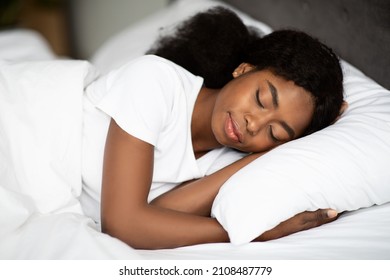 Closeup shot of peaceful young curly african american woman sleeping in comfortable bed alone at home, enjoying her high quality orthopedic mattress. Bedroom furniture, bedding concept