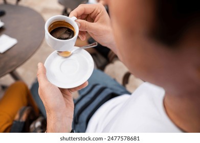 Close-up shot of a person holding a cup of espresso coffee with a saucer at an outdoor cafe, conveying relaxation and social vibes. - Powered by Shutterstock