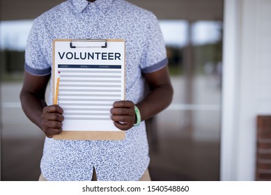 A Closeup Shot Of A Person Holding Up A Volunteer Sign Up Sheet With A Blurred Background