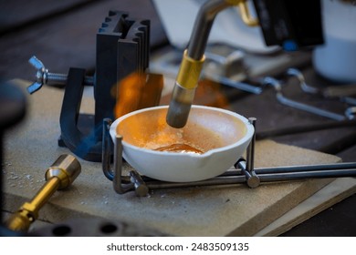 A close-up shot of a person melting silver in a small crucible using a propane torch, with a mold being heated in the background for casting. - Powered by Shutterstock