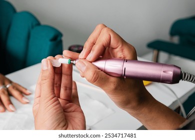 A close-up shot of a person using an electric nail drill to polish acrylic nails. The detailed view highlights the precision and care involved in professional nail care. - Powered by Shutterstock