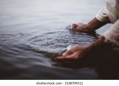A closeup shot of a person wearing a biblical robe washing his hands in the water