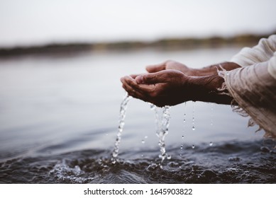 A closeup shot of a person wearing a biblical robe drinking water with hands