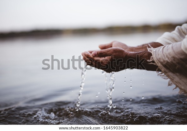 A closeup shot of a person wearing a biblical\
robe drinking water with\
hands