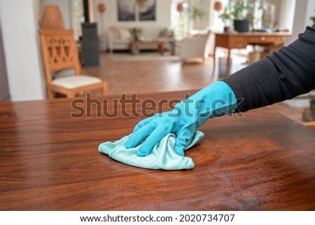A closeup shot of a person wearing gloves while sanitizing a woodensurface