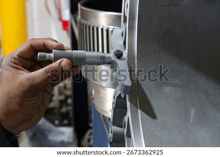 Close-up shot of a person's hands using a depth micrometer to precisely measure a large industrial metal component. The focus is on the intricate process of quality control.