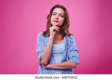 Close-up Shot Of Pretty Girl Thinking About The Plans Isolated Over Pink Background. Woman In Checked Shirt Standing In The Studio And Looking Upwards 