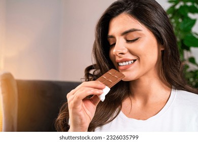 Closeup shot of pretty young Caucasian woman with long hair eating bar of chocolate and smiling  - Powered by Shutterstock