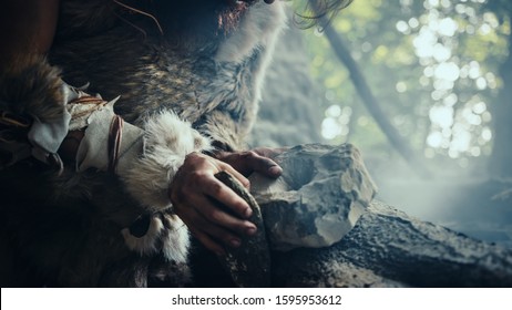 Closeup Shot of Primeval Caveman in Animal Skin Hits Rock with Sharp Stone, Makes First Primitive Tool for Hunting Animal Prey. Neanderthal Using Flint Rock. Dawn of Human Civilization.