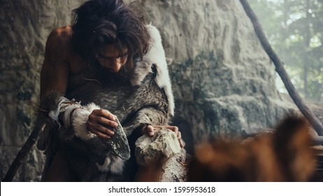 Close-up Shot of a Primeval Caveman Wearing Animal Skin Hits Rock with Sharp Stone, Makes First Primitive Tool for Hunting Animal Prey. Neanderthal Using Flint Rock. Dawn of Human Civilization.