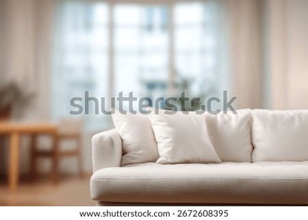 A close-up shot of a pristine white sofa adorned with plush white pillows, set against a softly blurred backdrop of a bright living room.