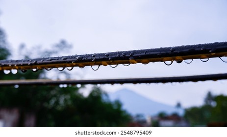 A close-up shot of rain droplets hanging on wires with a blurred mountain view in the background. The image captures the essence of tranquility and freshness after rainfall.  - Powered by Shutterstock