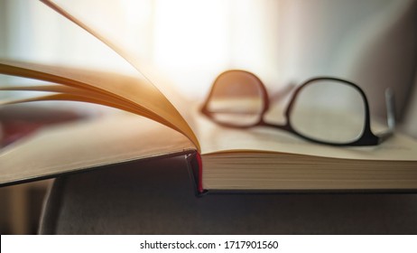 Closeup shot of reading glasses on an open book. Close up glasses and open book on the table. Book and glasses on a table in home interior. Book with eyeglasses on table in front of couch - Powered by Shutterstock