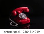 A closeup shot of a red vintage telephone with rotary dial